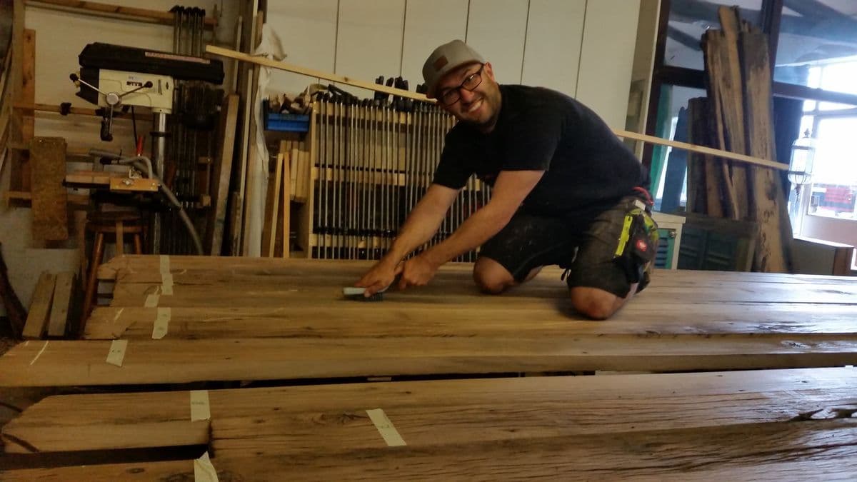 Milan Oesert in der Tischlerwerkstatt, kniend an Holzplanken