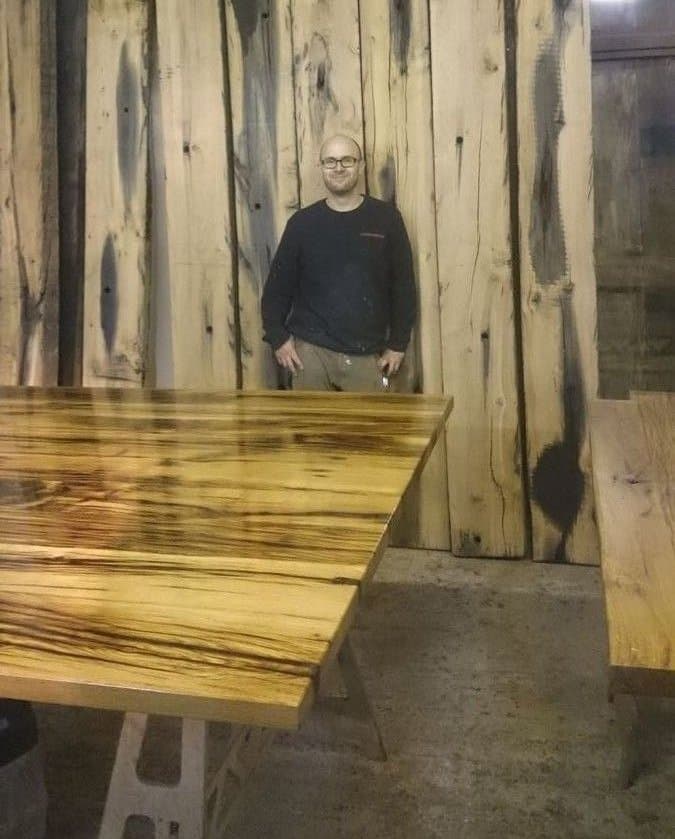 Milan Oesert vor massiven Holzplanken in der Tischlerwerkstatt